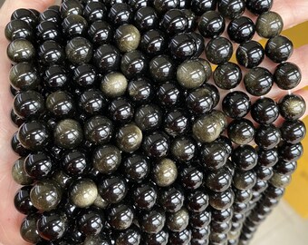 May include: A strand of black and gold beads with a shimmering, iridescent effect. The beads are round and smooth, and they are strung together on a clear thread.