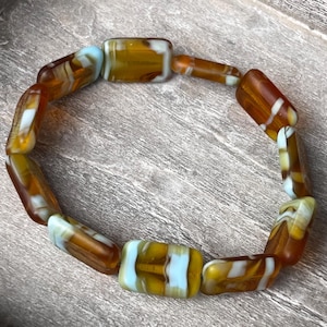 Könnte beinhalten: Ein Armband aus braunen und weißen Glasperlen. Die Perlen sind rechteckig und haben ein wirbelndes Muster.