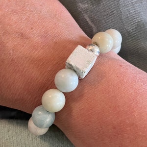 Könnte beinhalten: Ein Armband aus hellblauen und weißen Perlen mit einem weißen quadratischen Anhänger und silbernen Akzenten.