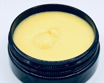 May include: A black jar filled with a pale yellow cream or lotion.