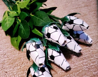 May include: A bouquet of artificial roses with a soccer ball pattern. The roses are white with black stitching and are arranged in a cluster.