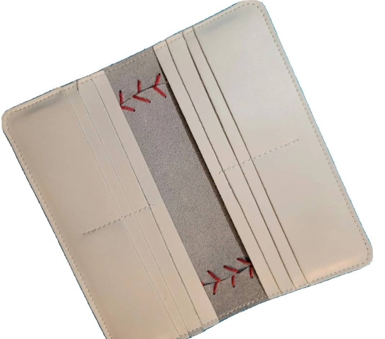 Pu&ograve; includere: Un portafoglio in pelle bianca con cuciture rosse, che ricorda una palla da baseball. Il portafoglio ha pi&ugrave; slot per carte e un porta banconote.