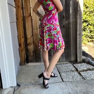 May include: A pink and green floral print dress with short sleeves and a fitted bodice. The dress has a flared skirt and is worn with black heeled sandals.