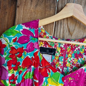 May include: A colorful floral print dress with a V-neckline and short sleeves. The dress has a zipper closure and a label that reads "Carole Little".
