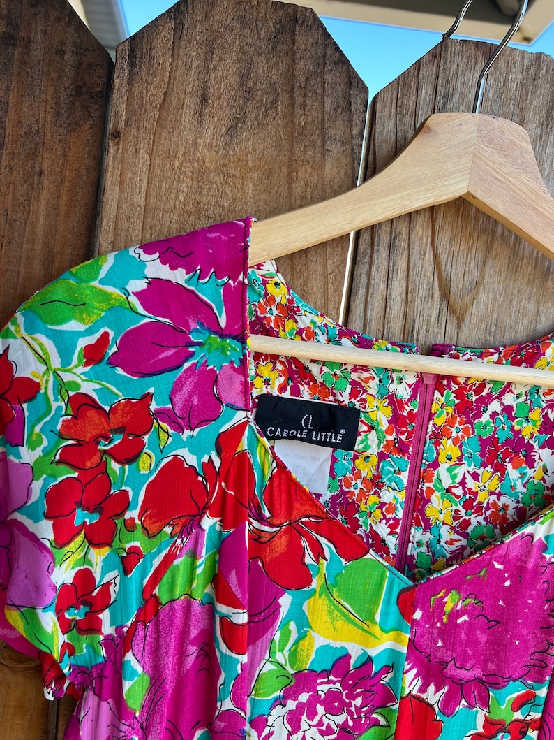 May include: A colorful floral print dress with a V-neckline and short sleeves. The dress has a zipper closure and a label that reads "Carole Little".