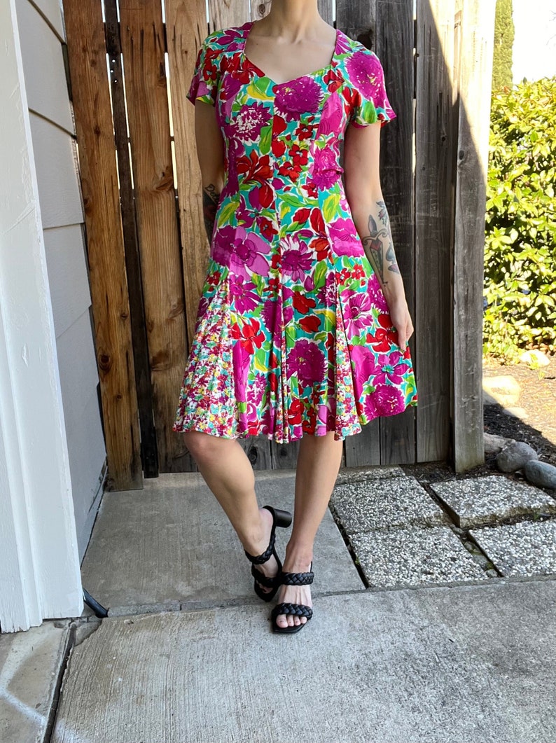 May include: A floral print dress with a pink, red, and green color scheme. The dress has a fitted bodice and a flared skirt. The dress is knee-length and has short sleeves.