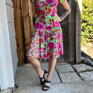 May include: A floral print dress with a pink, green, and red color scheme. The dress has a fitted bodice and a flared skirt. The dress is knee-length and has short sleeves.