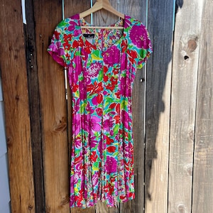 May include: A pink and green floral print dress with short sleeves and a scoop neck. The dress has a fitted bodice and a flowing skirt.