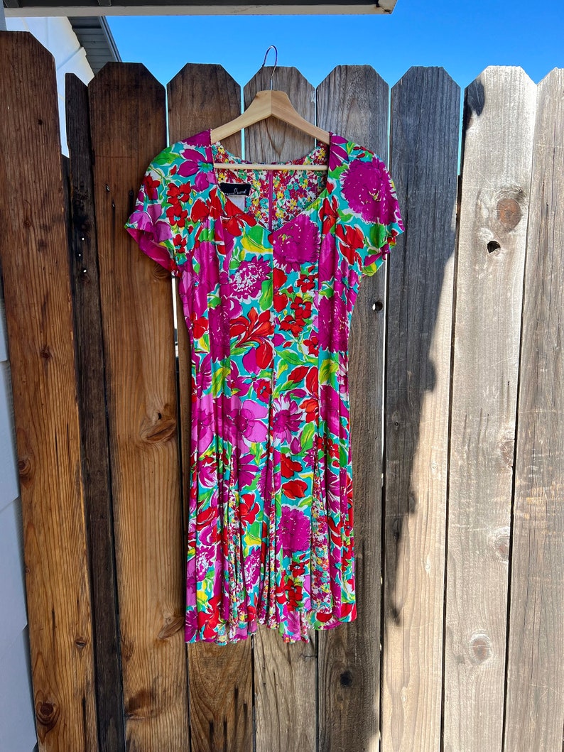 May include: A pink and green floral print dress with short sleeves and a scoop neck. The dress has a fitted bodice and a flowing skirt.