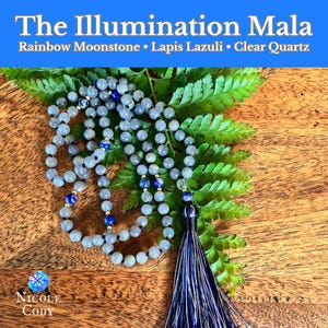 May include: A mala necklace with gray beads, blue lapis lazuli accents, and a navy tassel. The text "The Illumination Mala" is at the top, with "Rainbow Moonstone • Lapis Lazuli • Clear Quartz" below it. The necklace rests on green fern leaves.