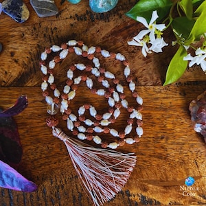 May include: A mala or prayer beads necklace with a tassel. The beads are white and brown and are strung on a cord. The tassel is white and brown and is made of a soft material.