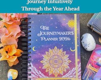 Puede incluir: Una agenda titulada "The Journeymaker's Planner 2026" con encuadernación en espiral y un diseño celestial. La portada presenta un mandala dorado y el texto "Journey Intuitively Through the Year Ahead." Otros elementos incluyen cartas del tarot, cristales y flores.