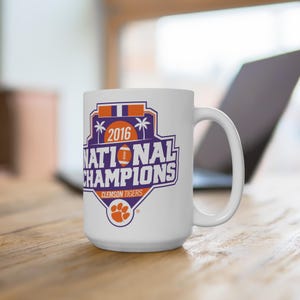 May include: White ceramic coffee mug with a purple and orange design that says "2016 National Champions Clemson Tigers".