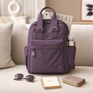 May include: A deep purple backpack with two top handles, a front zippered pocket, and side pockets. A clear water bottle is in the side pocket. A white paper with the text REAL is inside. A pair of sunglasses, a small notebook, and a wallet are in front.