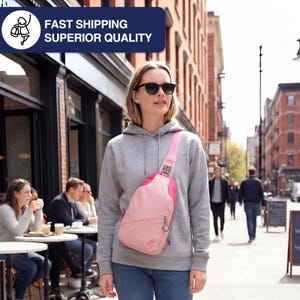 May include: A pink sling bag with a light pink strap and a silver-colored buckle. The bag has a zippered pocket and a small logo. The person in the image is wearing a gray hoodie and sunglasses.