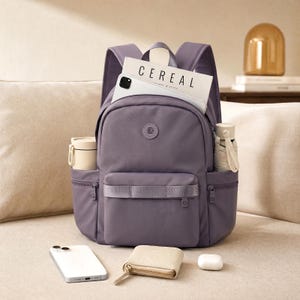 May include: A purple backpack with multiple pockets, holding a white phone, a magazine with the word "CEREAL", a small umbrella, and a thermos. A small wallet, a phone, and wireless earbuds are in front of the backpack.