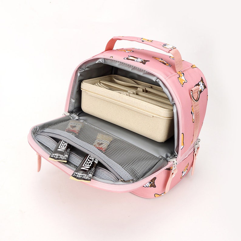 May include: Pink insulated lunch bag with a zipper closure and a handle. The bag has a print of cartoon dogs. The bag is open and shows a beige lunchbox inside, a mesh pocket, and two Nescafe sticks.