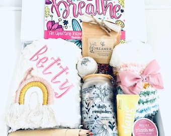 Può includere: Una scatola regalo bianca piena di articoli per la cura di sé, tra cui un libro da colorare intitolato "Positive Vibes Just Breathe", una bomba da bagno, un sale da bagno, una crema per le mani, uno scrub per il corpo, un set di matite colorate e una coperta di peluche ricamata con la parola "Betty".