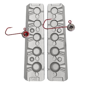 Könnte beinhalten: Eine zweiteilige Metallform zum Gießen von Angelköpfen. Die Form hat sechs Vertiefungen und ist mit "146" gekennzeichnet. Zwei fertige Jigköpfe mit roten Augen sind neben der Form abgebildet.