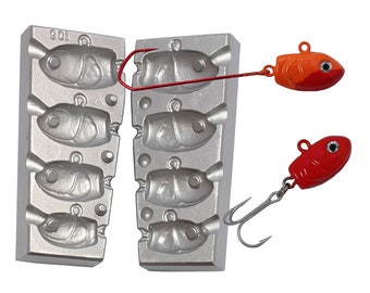 May include: A two-piece metal mould for casting fishing lures. The mould has six cavities shaped like fish. Two finished lures are shown, one red and one orange and red.