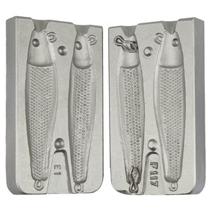 May include: Two-piece silver metal mold for casting fishing lures. The mold has two cavities, each with a detailed fish shape. The mold is labeled "E1" and "F117".