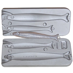 May include: A silver metal mold for making fishing lures. The mold has four cavities, each shaped like a fish. The mold is labeled "F1130".