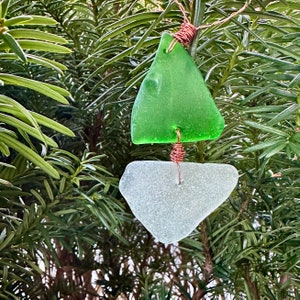 May include: A green and white glass sailboat ornament with copper wire accents. The ornament is hanging from a tree branch.