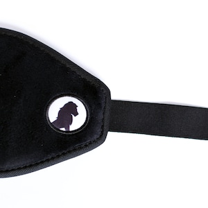 Puede incluir: M&aacute;scara para dormir negra con una textura suave y aterciopelada. La m&aacute;scara presenta un emblema circular con la silueta de un caballo. Una correa el&aacute;stica negra se extiende desde la m&aacute;scara.
