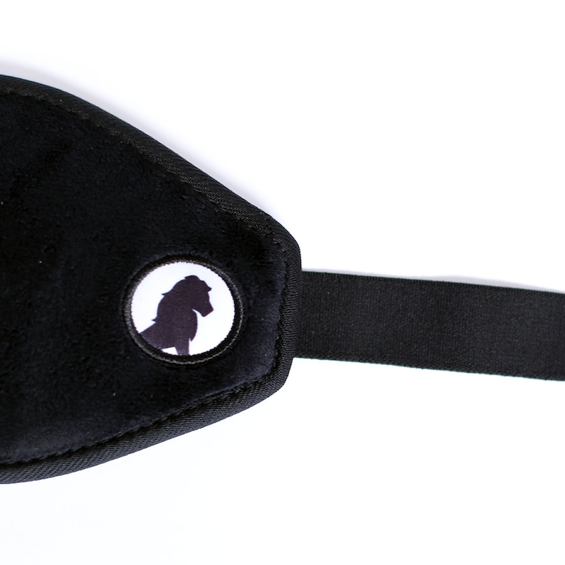 Puede incluir: M&aacute;scara para dormir negra con una textura suave y aterciopelada. La m&aacute;scara presenta un emblema circular con la silueta de un caballo. Una correa el&aacute;stica negra se extiende desde la m&aacute;scara.