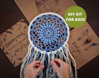 May include: A DIY kit for kids to make a dream catcher. The kit includes a white and blue crocheted dream catcher with white and blue feathers. The dream catcher is on a brown surface with a card that says "DIY KIT FOR KIDS!"
