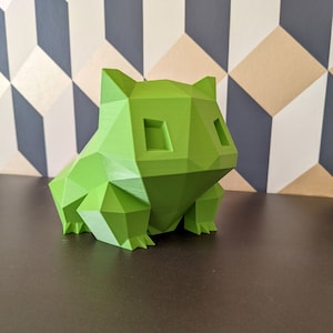 Peut inclure: Une figurine en 3D imprimée en vert, de style low-poly, représentant une grenouille de dessin animé. La figurine a un design simple et géométrique.