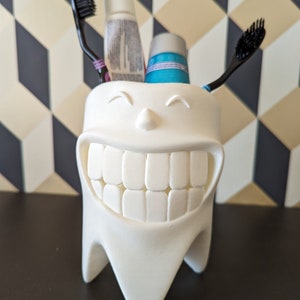 Peut inclure: Porte-brosses à dents en forme de dent blanche avec un visage souriant, contenant deux tubes de dentifrice et deux brosses à dents.