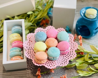 Puede incluir: Un encaje rosa con una variedad de macarons de color pastel. Los macarons están dispuestos en círculo sobre el encaje. También hay macarons en una caja blanca.