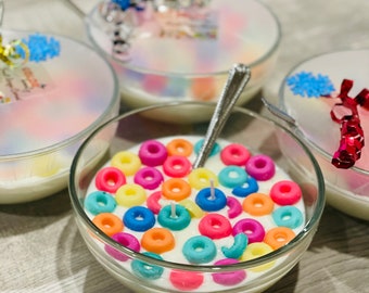 May include: Three glass bowls filled with white wax and colorful cereal-shaped candles. The bowl in the center has a silver spoon in it.