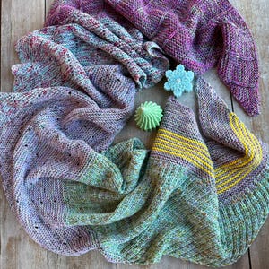 May include: A hand-knitted shawl in shades of purple, green, and yellow. The shawl is made with a variety of stitches and textures, creating a unique and interesting design.