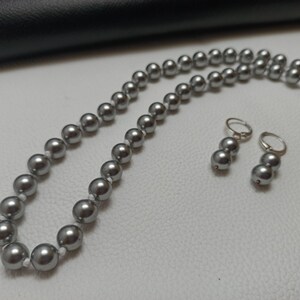 Vackert designerhalsband med grått pärlhalsband, örhängen med snäckskal, grå färg med snäckskalspärla och justerbar slitbana. Halsband, örhängen med set.