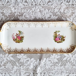 May include: A white porcelain serving tray with gold trim and two painted scenes of couples in a garden setting.