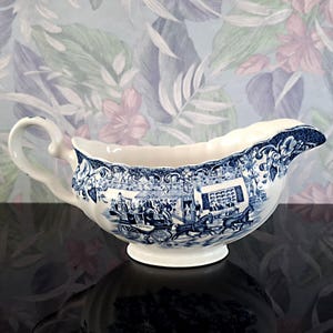 Peut inclure: Saucière en céramique blanche et bleue avec une anse et un bec verseur. Le bateau présente un motif bleu détaillé représentant une calèche et des personnages. Le bord a un bord festonné et le bateau repose sur une petite base ronde.