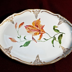 May include: A white oval serving tray with gold trim and a hand-painted orange lily flower design.