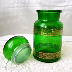 Peut inclure: Un pot en verre vert avec une bande décorative dorée autour du milieu. Le pot a un couvercle vert assorti.