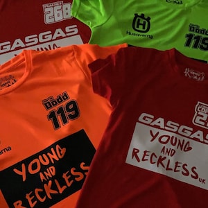 Può includere: Quattro magliette diverse con vari design e colori. Le magliette presentano il testo "GASGAS", "YOUNG AND RECKLESS", "PEACHEY 268" e "Husqvarna".