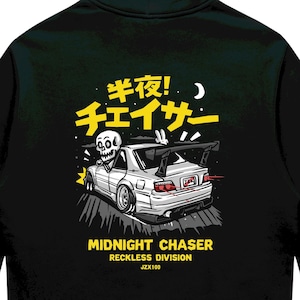 May include: A black hooded sweatshirt featuring a graphic on the back of a white sports car with a rear spoiler, driven by a skeleton. The design includes yellow Japanese text, a crescent moon, and the English text MIDNIGHT CHASER RECKLESS DIVISION JZX100.