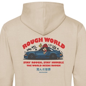 May include: Beige hoodie with a graphic on the back. The graphic features a blue car with a cartoon character and the text "ROUGH WORLD". Additional text includes "STAY ROUGH, STAY HUMBLE THE WORLD NEEDS ROUGH" and Japanese characters.
