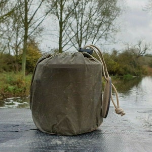 Puede incluir: Una bolsa de lona verde con cierre de cordón y una etiqueta de cuero. La bolsa está sobre una superficie de madera.