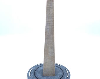 Könnte beinhalten: Ein Miniaturmodell des Washington Monument. Das Denkmal ist eine hohe, rechteckige Struktur mit einer spitzen Spitze, die Ziegeln nachempfunden ist. Es steht auf einem kreisförmigen Sockel mit den weißen Worten "WASHINGTON DC".