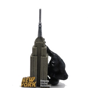 Puede incluir: Una figurita de gorila negro escalando el Empire State Building, una réplica en miniatura del famoso rascacielos de la ciudad de Nueva York. La figurita está hecha de plástico y tiene un diseño detallado. La base de la figurita tiene las palabras "New York" y "Empire State Building" impresas.