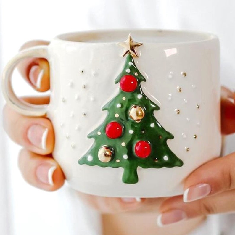 May include: White ceramic mug with a 3D green Christmas tree design. The tree has red and gold ornaments and a gold star on top.