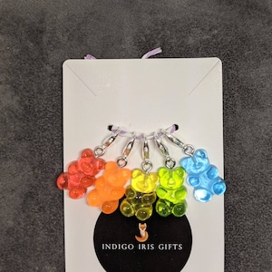 Puede incluir: Conjunto de seis marcadores de punto de osito gominola arco&iacute;ris con anillos plateados. Los ositos gominola son rojo, naranja, amarillo, verde, azul y morado. Los marcadores de punto est&aacute;n etiquetados con "INDIGO IRIS GIFTS".