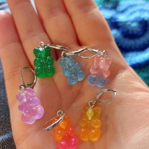 Puede incluir: Seis pendientes con forma de osito de goma en varios colores, incluyendo verde, azul, rosa, naranja y rojo. Los pendientes est&aacute;n unidos a ganchos de pendientes plateados.