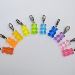Puede incluir: Diez abalorios con forma de osito de goma de colores con cierres plateados. Los abalorios est&aacute;n dispuestos en forma de arco&iacute;ris, comenzando por el naranja y terminando por el rosa.